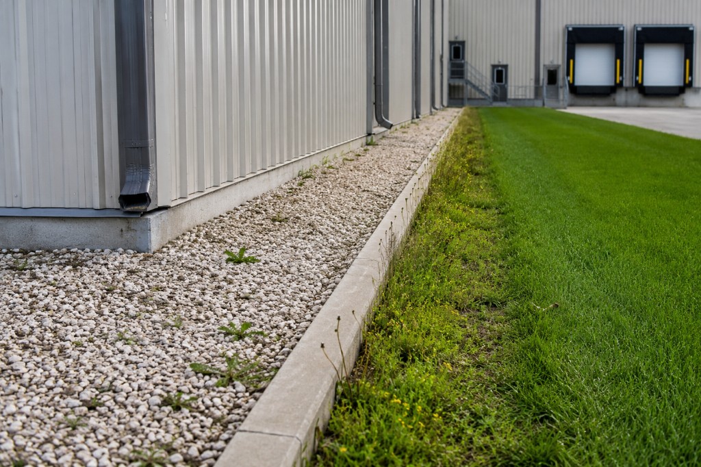 Technician applying perimeter weed treatment along a facility exterior